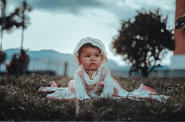 niña en el suelo celebrando bautizo, gorro, niña pequeña